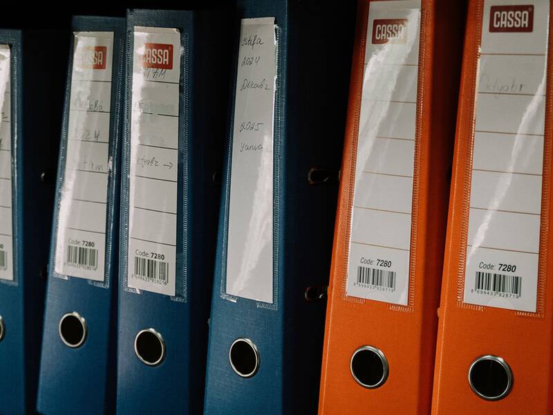 Mehrere blaue und orangefarbene Ordner stehen aufrecht nebeneinander in einem Regal.