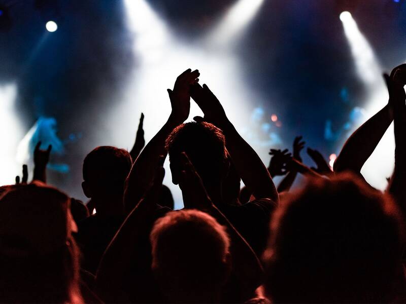 Eine Menschenmenge bei einem Konzert klatscht begeistert vor einer bunt beleuchteten Bühne.
