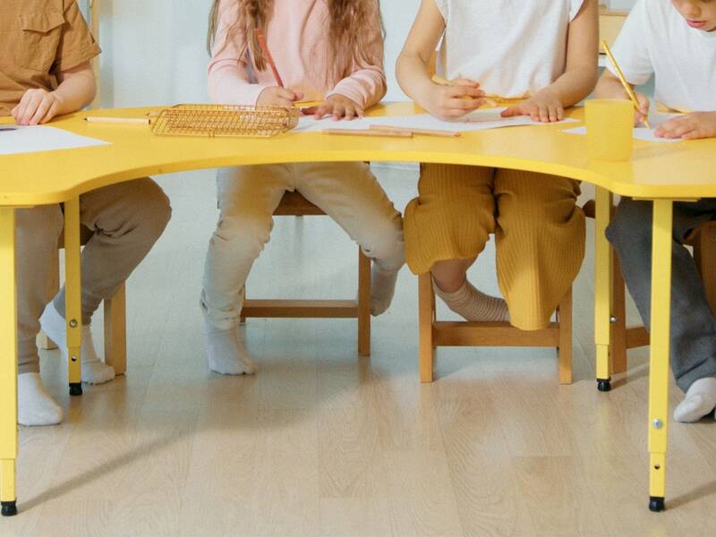 Vier Kinder sitzen an einem gelben Tisch und zeichnen auf Papier.