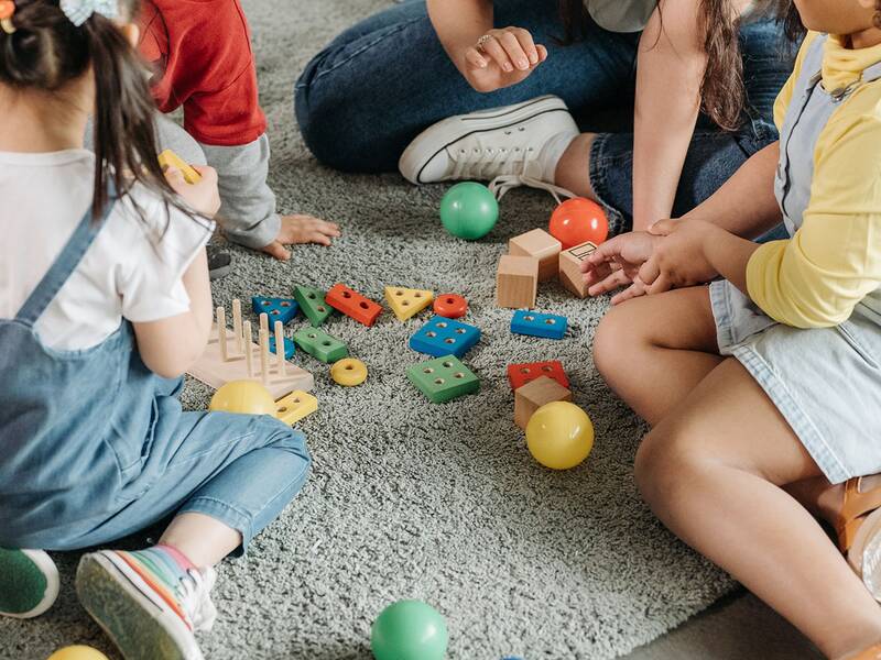 Kinder sitzen auf einem Teppich und spielen mit bunten Bauklötzen und Bällen.