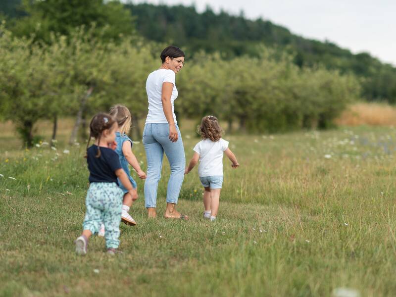 Eine Frau und drei Kinder laufen barfuß über eine Wiese bei sommerlichem Wetter.