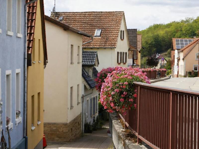 Eine malerische Dorfstraße mit bunten Häusern und einem blühenden Blumenkorb am Geländer.