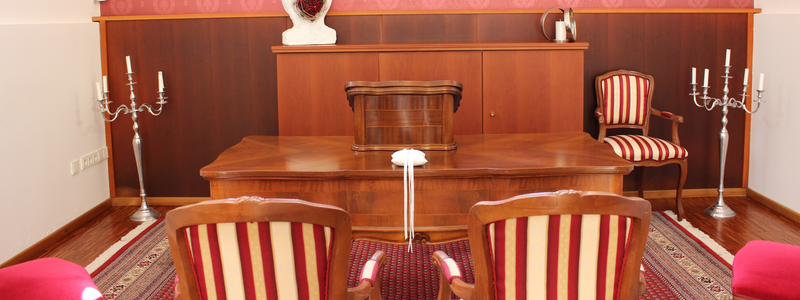 Der Raum ist elegant dekoriert mit rot-weiß gestreiften Stühlen, einem hölzernen Tisch und Schrank, einer roten Tapete, drei Kerzenständern und einer weißen Skulptur auf einem Regal.