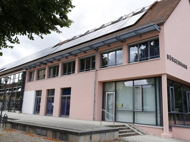 Ein modernes Gebäude mit großen Fenstern und Solarpanelen auf dem Dach trägt die Aufschrift "Bürgerhaus".