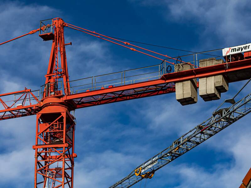 Ein roter Baukran steht vor einem blauen Himmel, und an einem Teil des Krans sind Betonblöcke befestigt.