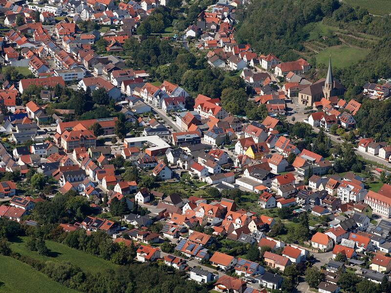 Luftaufnahme eines Dorfes mit vielen rot gedeckten Häusern, einer Kirche und umgeben von Grünflächen.