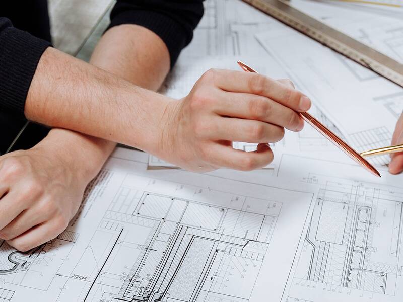 Zwei Personen besprechen Architekturzeichnungen auf einem Tisch und halten dabei Stifte in den Händen.